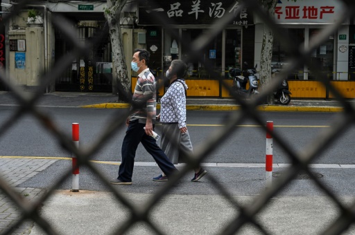 Des piétons passent devant les grilles d'un ensemble résidentiel sous confinement, le 19 mai 2022 à Shanghai
